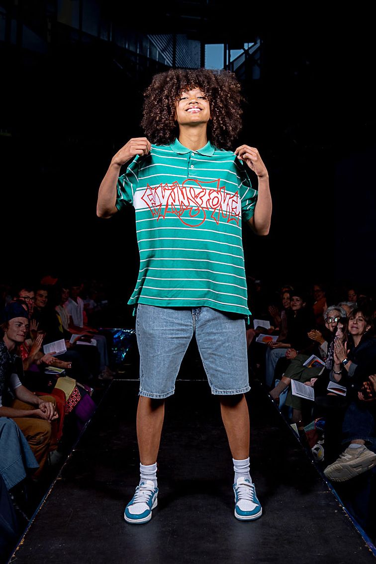Student modeling for the CC Fashion Show wearing a striped, collared blue t-shirt with graffiti words and denim shorts.