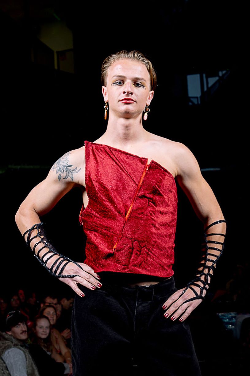 Student modeling for the CC Fashion Show wearing a bright red one-shoulder top with strappy arm pieces. 