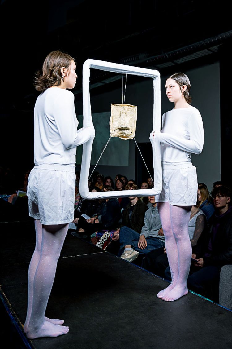 2 students modeling for the CC Fashion Show wearing all-white clothing and holding a frame with a dirty fabric within.