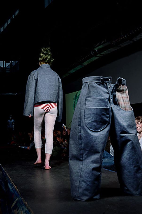 Student modeling for the CC Fashion Show wearing a denim jacket, white tights, and red and white bikini bottom. They are walking away from a freestanding pair of denim jeans.