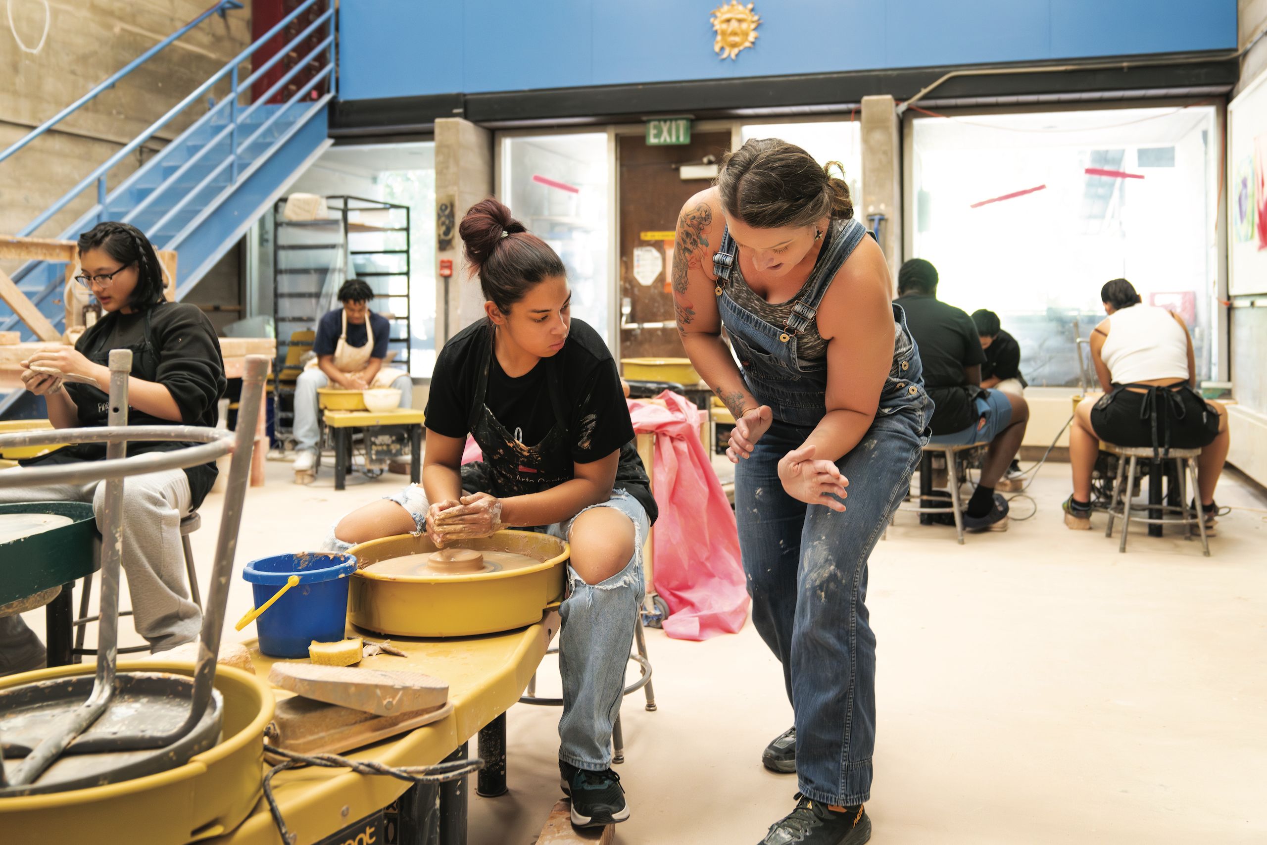Community volunteer Nitra Olsen demonstrates to Ati Marrow, sophomore at Sand Creek High School, during the Stroud Scholars class wheel throwing in the clay studio in the Bemis Art School. 