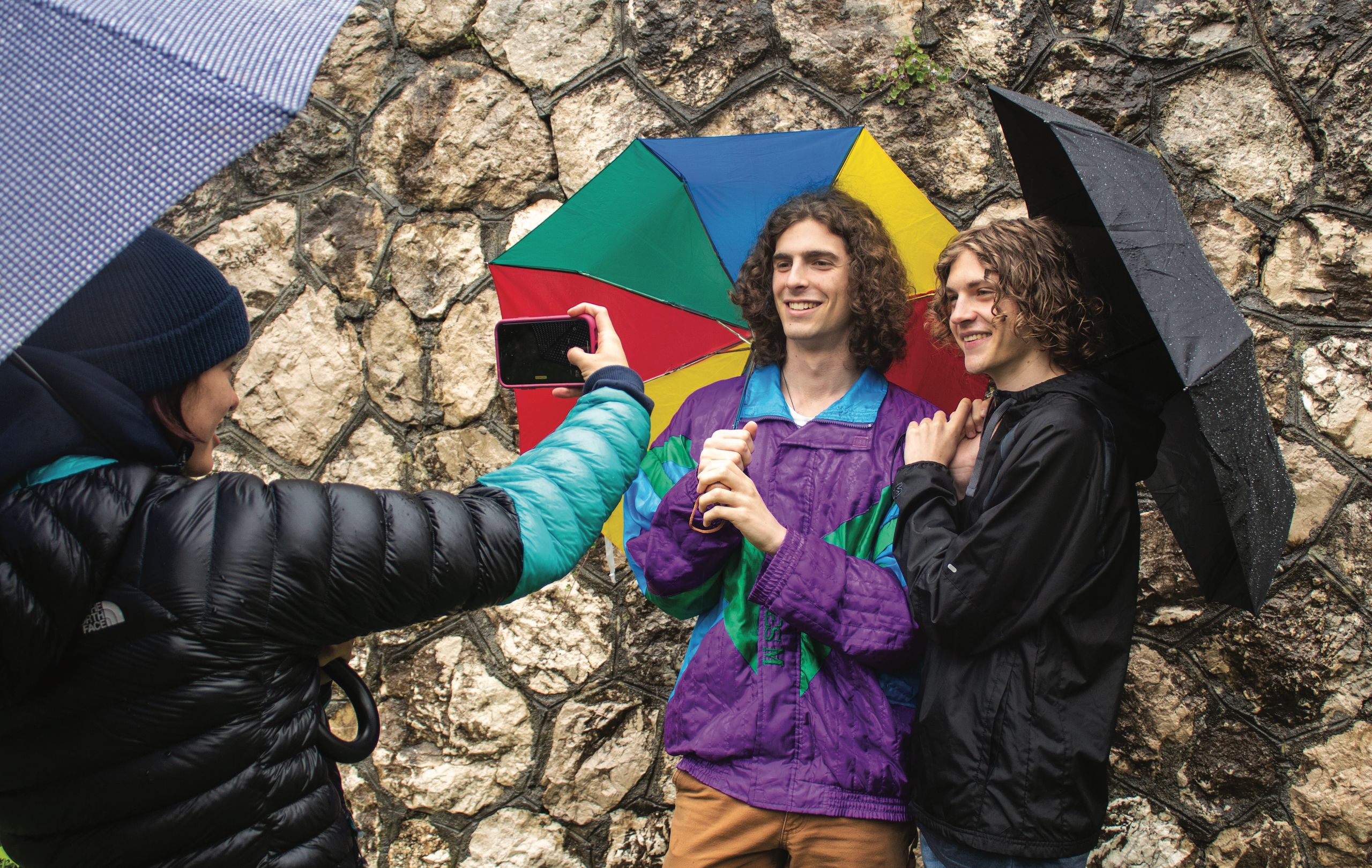 Two students with umbrellas pose for a photo in front of a wall in Villetta Barrea.