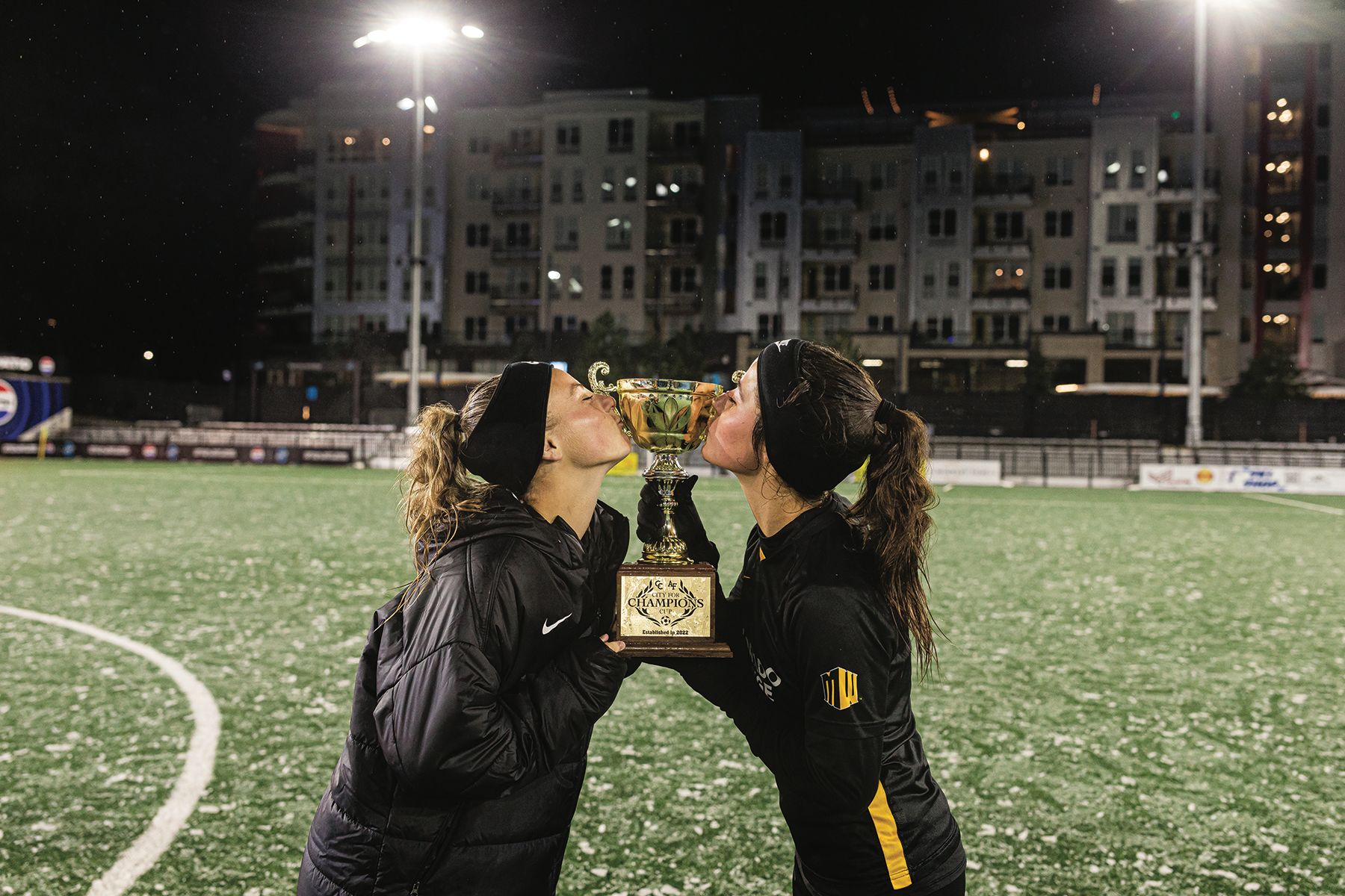 Two players on the Colorado College Women's Soccer team kissing the City of Champions trophy on the field