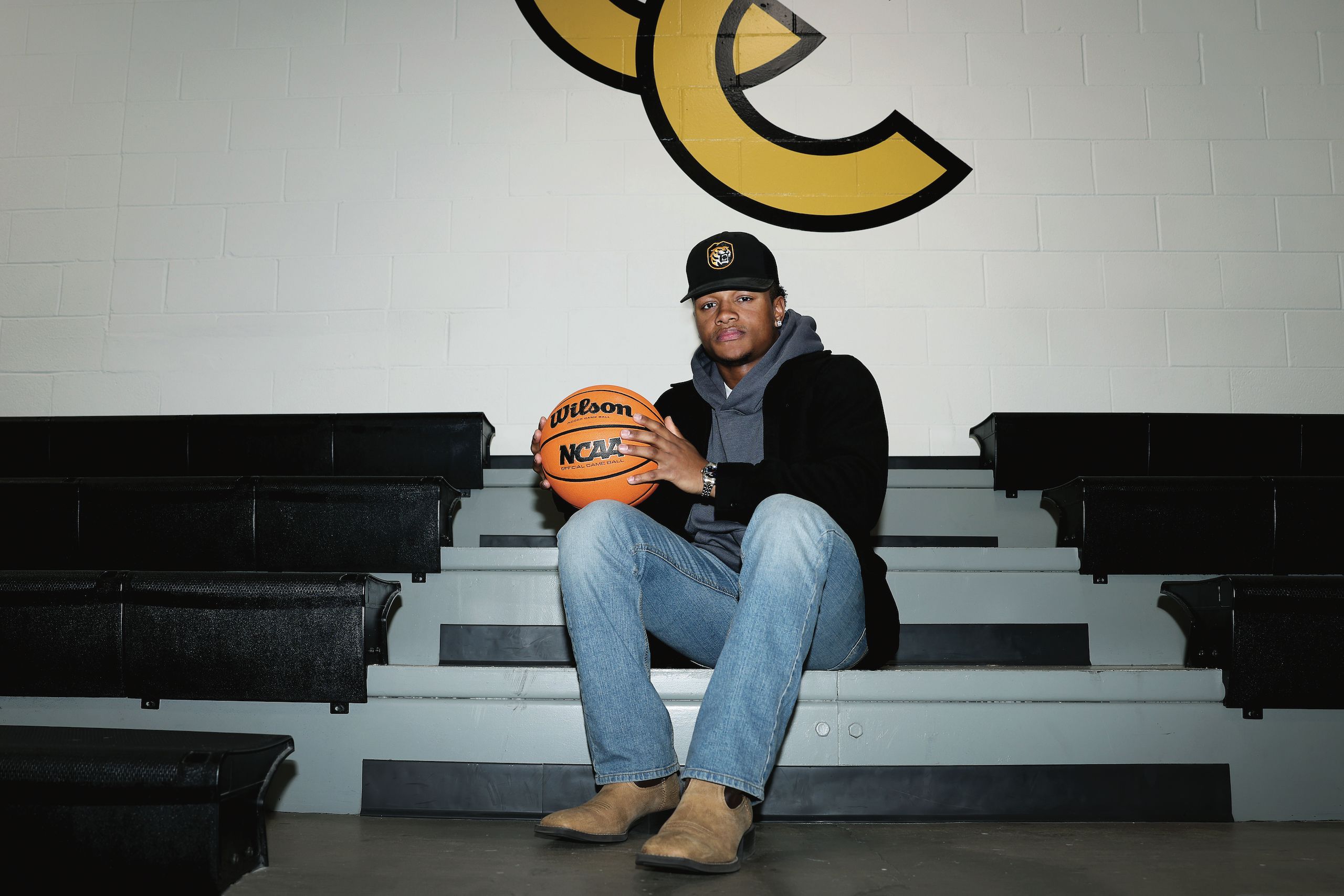 Kenney Andrews '26, a CC basketball player, sits on the benches in street clothes holding a basketball