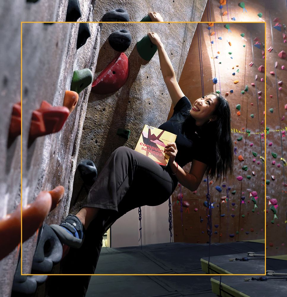 Primer Hour '25 holding a computer science book while rock climbing at the Ritt Kellogg Climbing Gym.